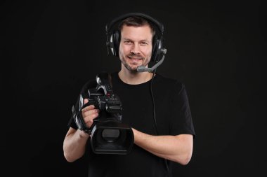 Profesyonel kameralı ve kulaklıklı bir adam siyah arka planda.