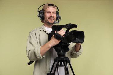 Profesyonel kamera ve soluk zeytinli arka planda kulaklığı olan bir adam.