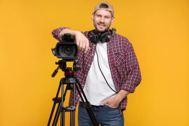 Profesyonel kamera ve turuncu arka planda kulaklığı olan bir adam.