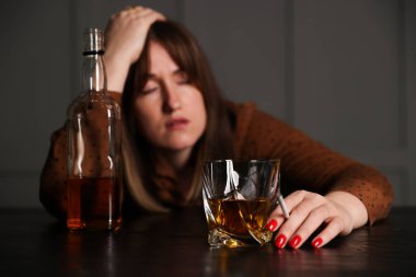 Alkol bağımlılığı. Bir bardak viskisi, sigarası ve şişesi olan bir kadın içeride, seçici bir odak noktası var.