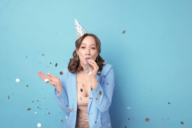 Doğum günü kutlaması. Açık mavi arka planda parti kornosu ve konfetisi olan bir kadın.