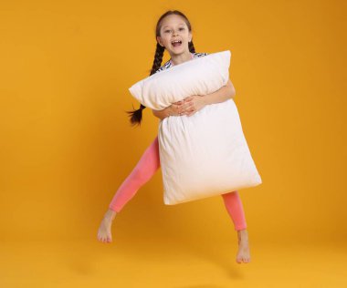 Turuncu arka planda yastıkla zıplayan tatlı kız.