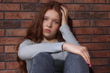 Evdeki tuğla duvarın yanındaki üzgün genç kız.