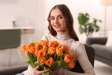 Evdeki koltukta bir buket lale ile gülümseyen kadın.