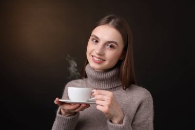 Kahverengi arka planda bir fincan kahveyle gülümseyen kadın.