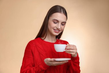 Bej renkli arka planda bir fincan kahveyle gülümseyen kadın