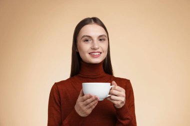 Bej renkli arka planda bir fincan kahveyle gülümseyen kadın