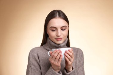 Bej renkli arka planda fincandan kahve içen kadın