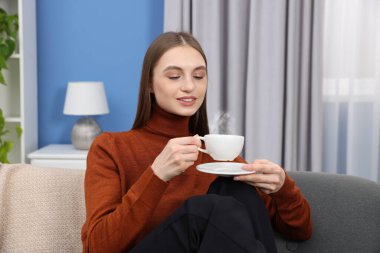 Evdeki kanepede bir fincan kahveyle gülümseyen kadın.
