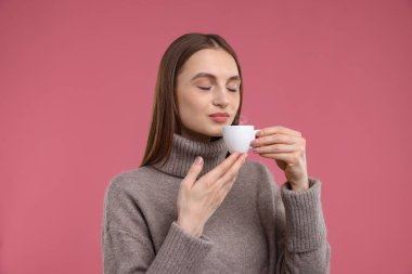 Pembe arka planda bir fincan kahvesi olan kadın.