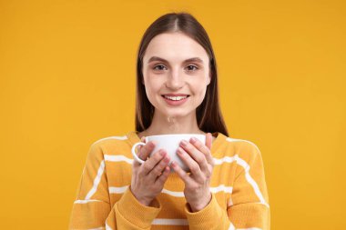 Sarı arka planda bir fincan kahveyle gülümseyen kadın.