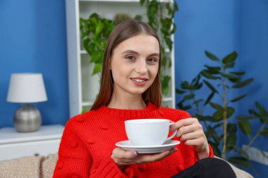 Evde bir fincan kahveyle gülümseyen kadın.