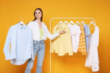 Gülümseyen moda tasarımcısı ve sarı arka planda giysileri olan askılar.