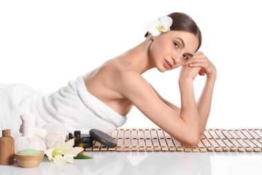 Beyaz arka planda bambu hasırında poz veren güzel bir kadın. Ayna yüzeyinde kaplıca ürünleri ve çiçekler