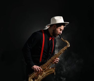 Profesyonel müzisyen siyah arkaplanda dumanla saksafon çalıyor.
