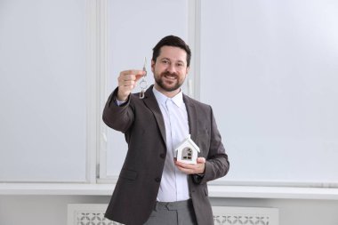 Emlakçının elinde anahtarlık ve ev modeli var.