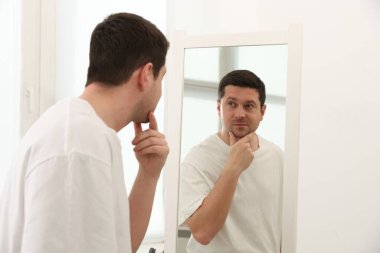 Yakışıklı adam aynada kendine bakıyor.