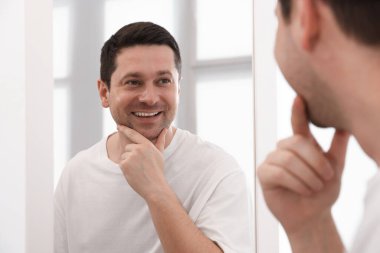 Yakışıklı adam aynada kendine bakıyor.