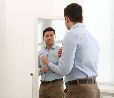 Yakışıklı adam aynada kendine bakıyor.