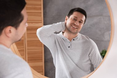 Yakışıklı adam aynada kendine bakıyor.