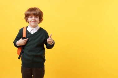 Sırt çantalı yakışıklı okul çocuğu sarı arka planda baş parmak gösteriyor, mesaj için yer var.