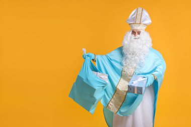 Turuncu arka planda bir çanta dolusu Noel hediyesiyle Aziz Nicholas, mesaj için yer