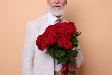 Bej arka planda kırmızı gül buketi olan yaşlı adam, yakın plan.