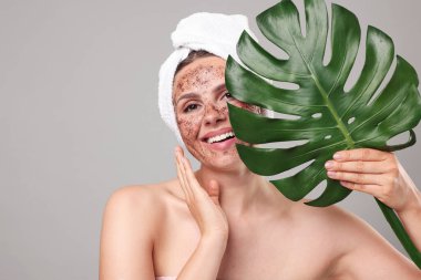 Yüzünde vücut fırçası ve gri arka planda canavar yaprağı olan gülümseyen bir kadın. Metin için boşluk