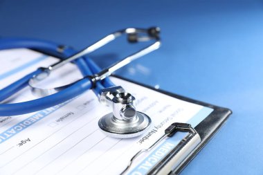 Mavi arka planda steteskop ve tıbbi kart formu, yakın plan.