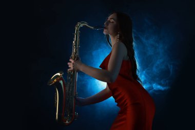 Profesyonel müzisyen koyu arkaplanda mavi ışık ve dumanla saksafon çalıyor.