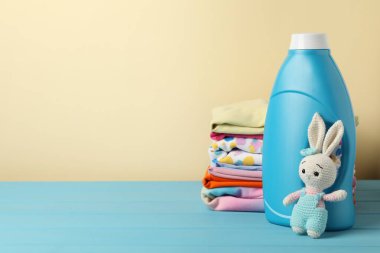 Kumaş yumuşatıcı, bebek kıyafetleri ve bej arka planda açık mavi ahşap masada oyuncak. Metin için boşluk