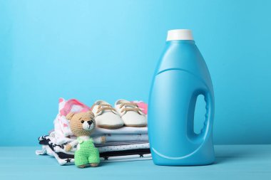 Şişe yumuşatıcı, bebek kıyafetleri ve açık mavi ahşap masada oyuncak.