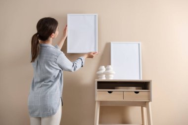 Bej duvarda boş bir çerçeve asılı kadın, arka manzara