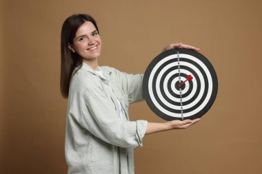 Hedef alınıyor. Bej arka planda ok ve dart tahtası olan gülümseyen kadın.