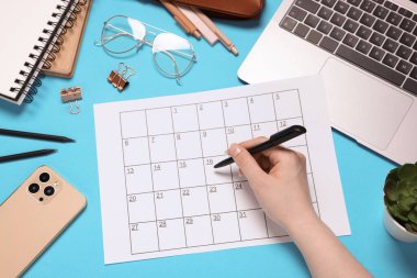 Planlayıcısı, kırtasiyesi, dizüstü bilgisayarı ve açık mavi arka planda akıllı telefonu olan kadın.