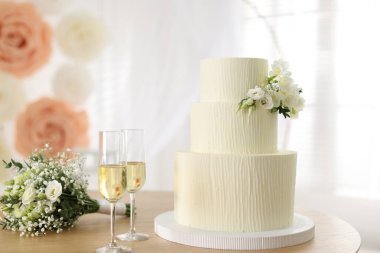 Çiçek desenli nefis düğün pastası, şampanya bardakları ve ahşap masa üzerindeki buket.