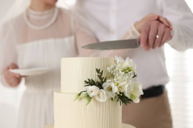 Evli çift içeride bıçakla lezzetli bir düğün pastası kesiyor.