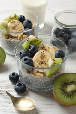 Chia tohumlu lezzetli tatlı, yoğurt, granola, yaban mersini, muz ve kivi beyaz ahşap masada, yakın plan. Süper yemek.