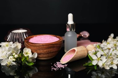 Kozmetik ürünleriyle kaplıca kompozisyonu, yanan mum ve siyah ayna yüzeyinde güzel çiçekler, yakın plan.