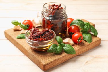 Lezzetli güneşte kurutulmuş domatesler, taze sebzeler, fesleğen ve sarımsak beyaz ahşap masada, yakın plan.