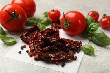 Lezzetli güneşte kurutulmuş domatesler, taze sebzeler ve baharatlar gri desenli masada, yakın plan.