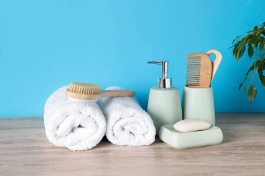 Açık mavi arka planda, ahşap masadaki farklı banyo aksesuarları.