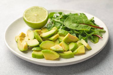 Olgun yeşil avokado, yeşil yeşiller ve açık gri masada limon, yakın plan.