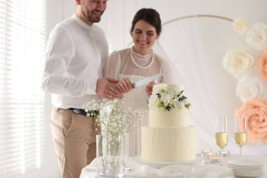 Evli çift evde bıçakla düğün pastası kesiyor, seçici bir odak noktası var.