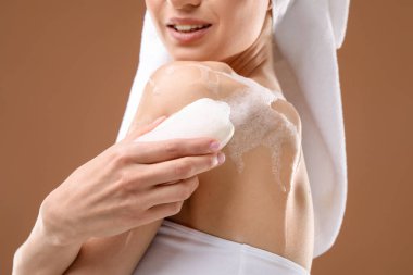 Kahverengi arka planda sabunla vücudu yıkayan gülümseyen kadın, yakın plan.