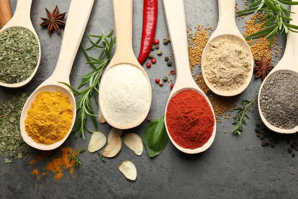 Gri masadaki kaşıklardaki farklı baharatlar düzdü.