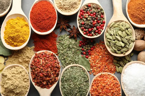 Gri masadaki kaşıklardaki farklı baharatlar düzdü.