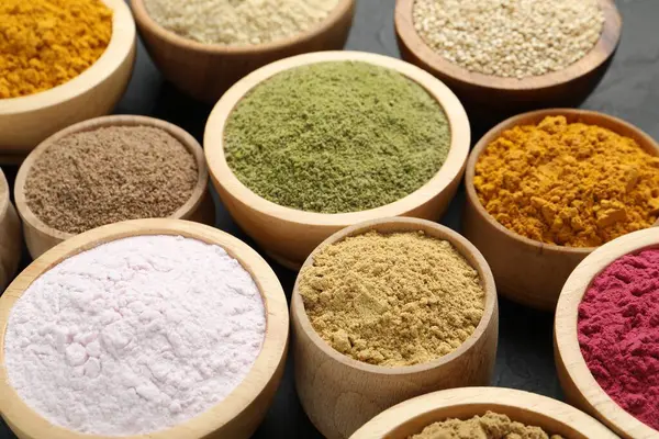 Karanlık masadaki kaselerde farklı süper yiyecek tozları, yakın plan.