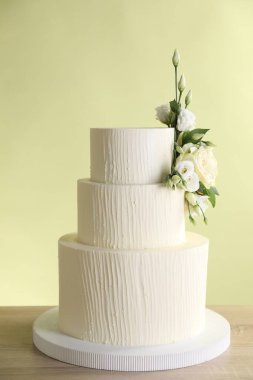 Ahşap masada çiçeklerle süslenmiş nefis bir düğün pastası açık yeşil arka planda, yakın plan.