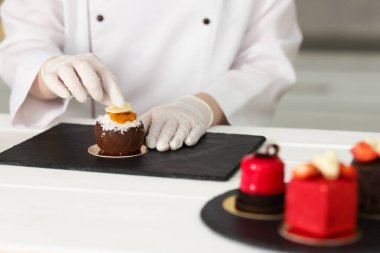 Mutfaktaki beyaz ahşap masada lezzetli bir tatlıyı dekore eden şekerci, yakın plan.